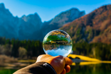 Hand hält Glaskugel, die eine Berglandschaft auf den Kopf gestellt spiegelt