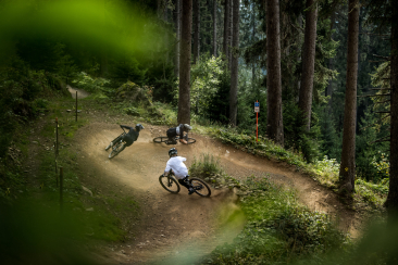 Drei Mountainbiker fahren mit viel Flow durch eine geschwungene Kurve im Wald des Bike Kingdom Parks Lenzerheide