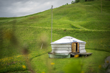 Runde Jurte mit Holztür auf einer Wiese inmitten grüner Hügel.