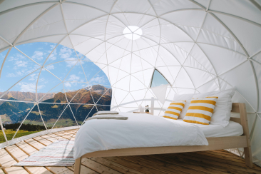 Gemütlicher Glamping-Dome mit Bett und Blick auf sonnige Berglandschaft