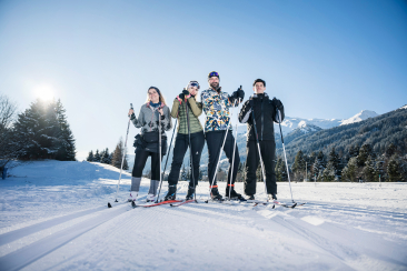 Vier junge Menschen beim Langlaufen auf der Loipe in Graubünden vor verschneiter Bergkulisse