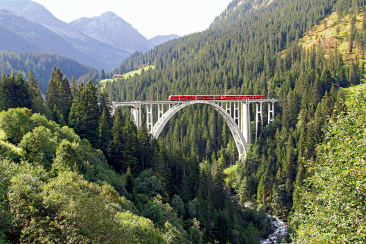 Un treno regionale rosso della Ferrovia retica attraversa in estate il viadotto di Langwies