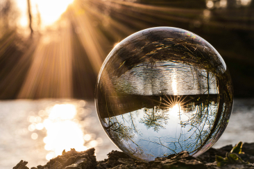 Glaskugel am Ufer im Sonnenlicht, spiegelt Landschaft und Lichtstrahlen