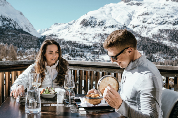 Paar beim Essen auf der Sonnenterrasse des Nira Alpina in Silvaplana mit Blick auf die verschneiten Berge