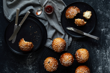 Frisch gebackene Bündner Bütschella mit Hagelzucker, serviert mit Butter und Konfitüre auf schwarzen Tellern.