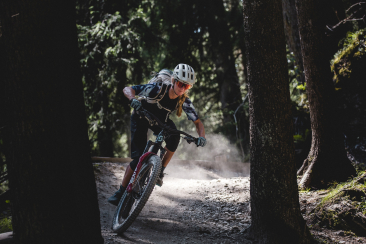 Bikerin unterwegs auf dem Runca Trail in Flims Laax umgeben von Baumstämmen.