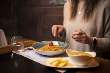 Woman eating a plate of traditional Graubünden Maluns served with alpine cheese and apple sauce at the restaurant of Hotel Stern in Chur