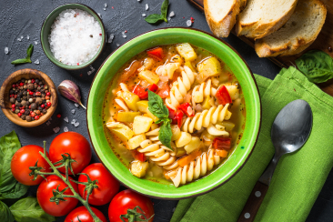 Grüne Schale mit Nudelsuppe, frischen Tomaten, Gewürzen und Brot auf dunklem Tisch