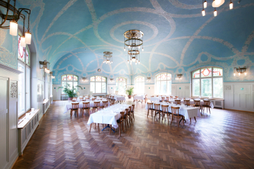 Salle historique de style Art nouveau avec voûte bleue et lustres ainsi que des tables dressées au Kurhaus Bergün