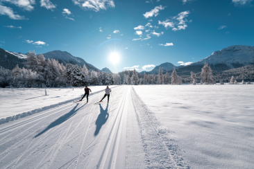 Zwei Personen beim Langlaufen auf einer sonnigen Loipe im Engadin