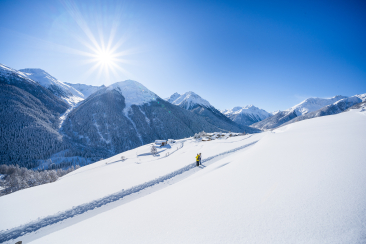 Zwei Winterwanderer auf dem präparierten Winterwanderweg der Via Engiadina mit Blick auf das verschneite Bergdorf Guarda