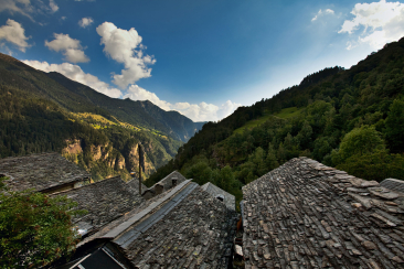 Traditionelle Häuser mit Steinplattendächern im Bergdorf Landarenca, eingebettet in die alpine Landschaft des Calancatals