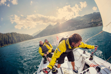 Three men with life jackets on a sailing boat on Lake St. Moritz